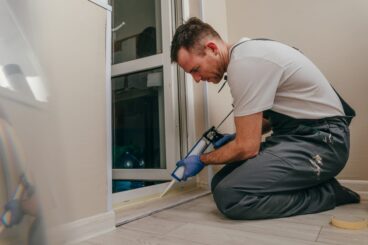 Young,Man,Wearing,Overalls,Sealing,Cracks,Between,Door,And,Trim